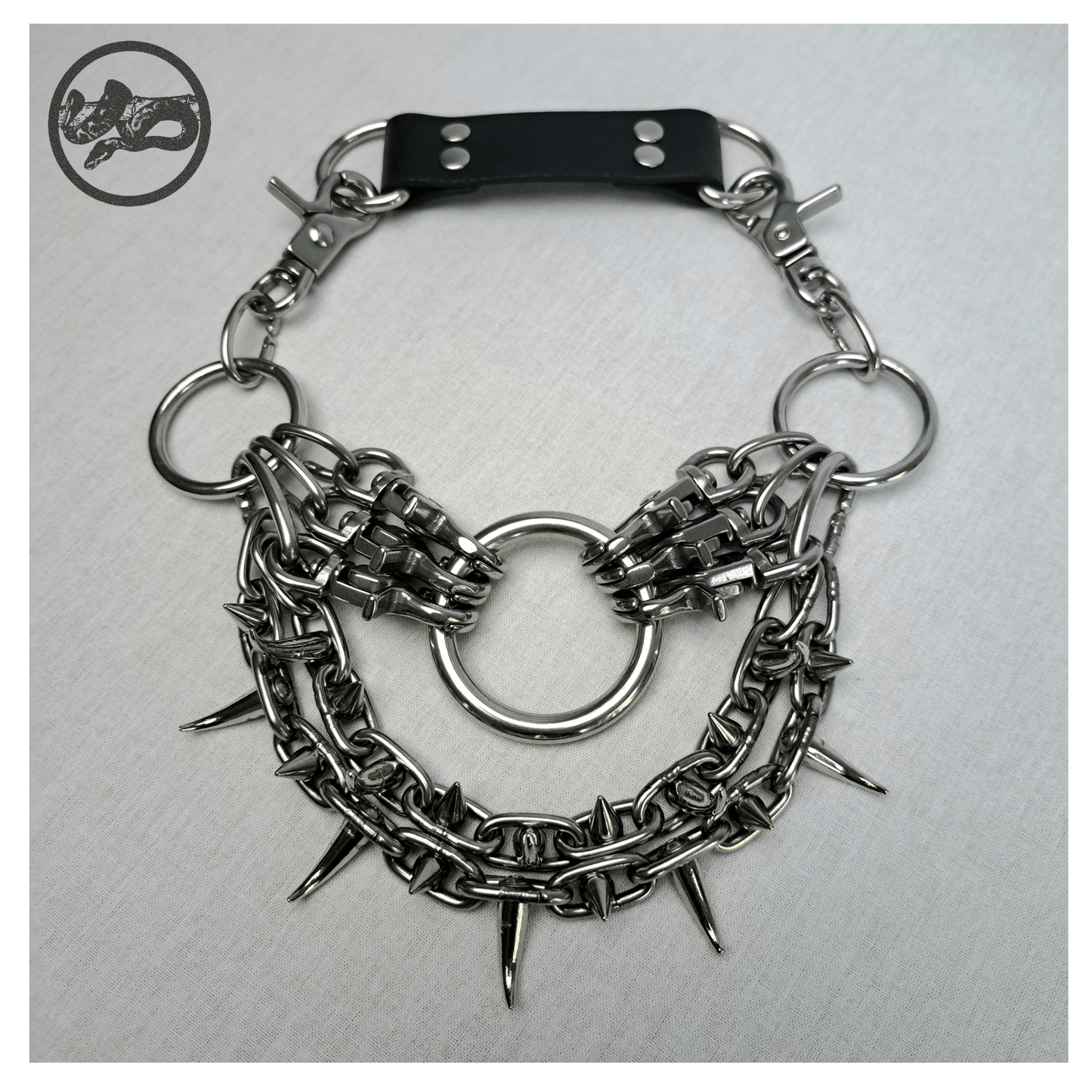 ChatGPT said:
FEGEFLAMME brutalist necklace laid out on a white background, front view showing studded stainless steel chains with small zinc alloy claw spikes, central O-ring, and reclaimed leather neckpiece secured with stainless steel carbines — gothic handcrafted accessory by skinpressedtight.