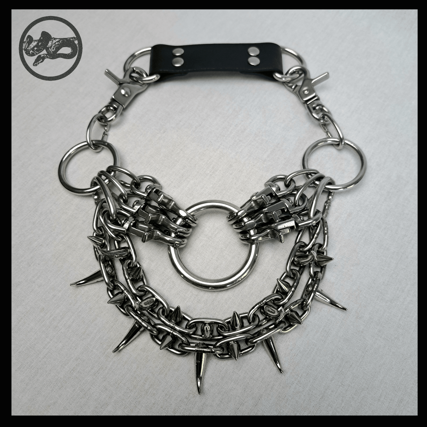 FEGEFLAMME brutalist necklace laid out on a white background, front view showing studded stainless steel chains with small zinc alloy claw spikes, central O-ring, and reclaimed leather neckpiece secured with stainless steel carbines — gothic handcrafted accessory by skinpressedtight.