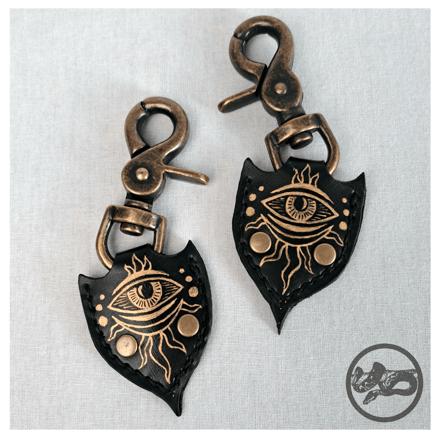 JOTKAELL spearhead-shaped earrings and ear charms laid out on a white background, front view showing leather pieces with handpainted golden eyes and tentacle ornaments, attached with brass carbines — gothic handcrafted accessories by skinpressedtight.