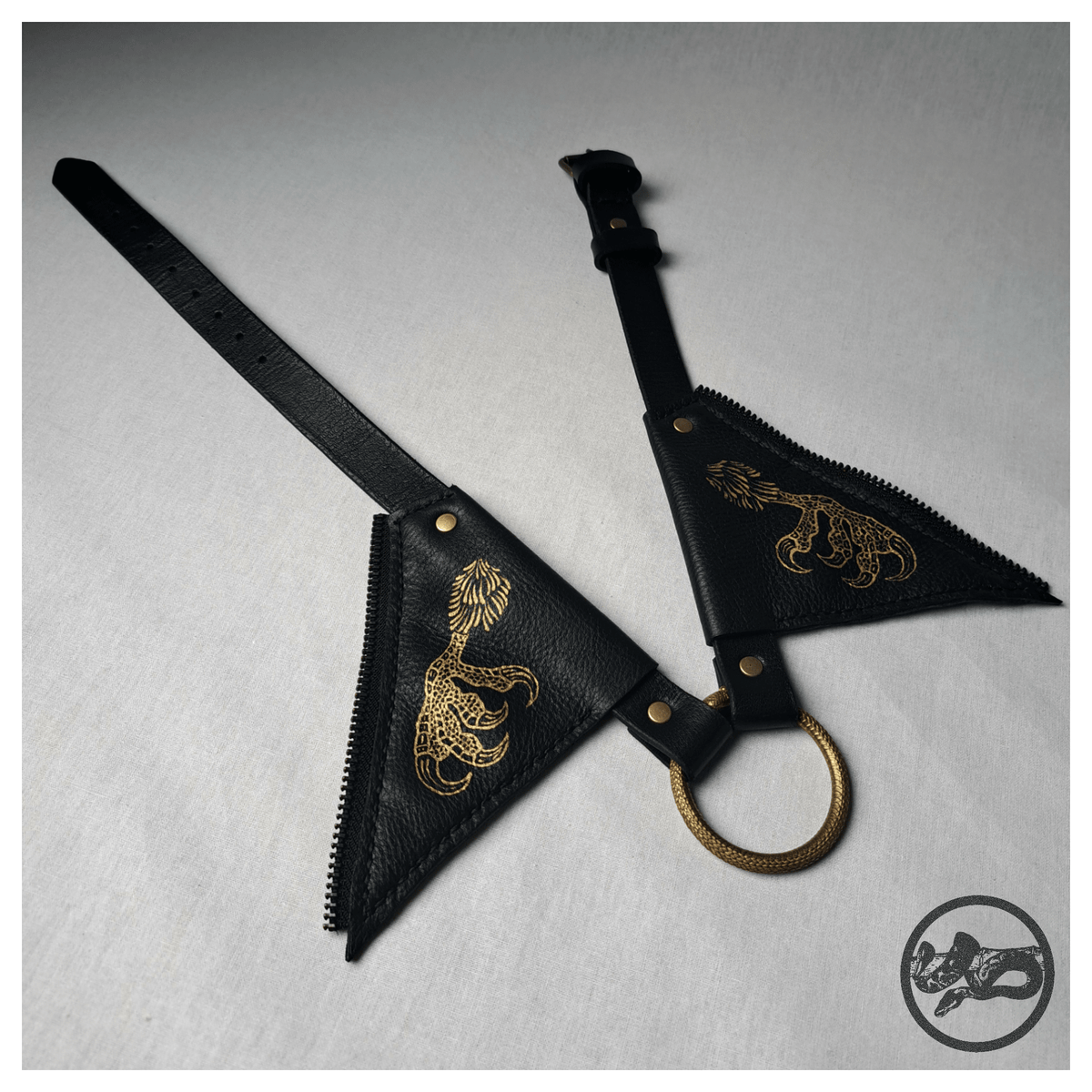 FLATTERTIER – BABA JAGA leather collar necklace laid out open: the two flaps painted with gold chicken feet, the brass snake ring and the black strap with an antique-brass roller buckle. Handmade by skinpressedtight