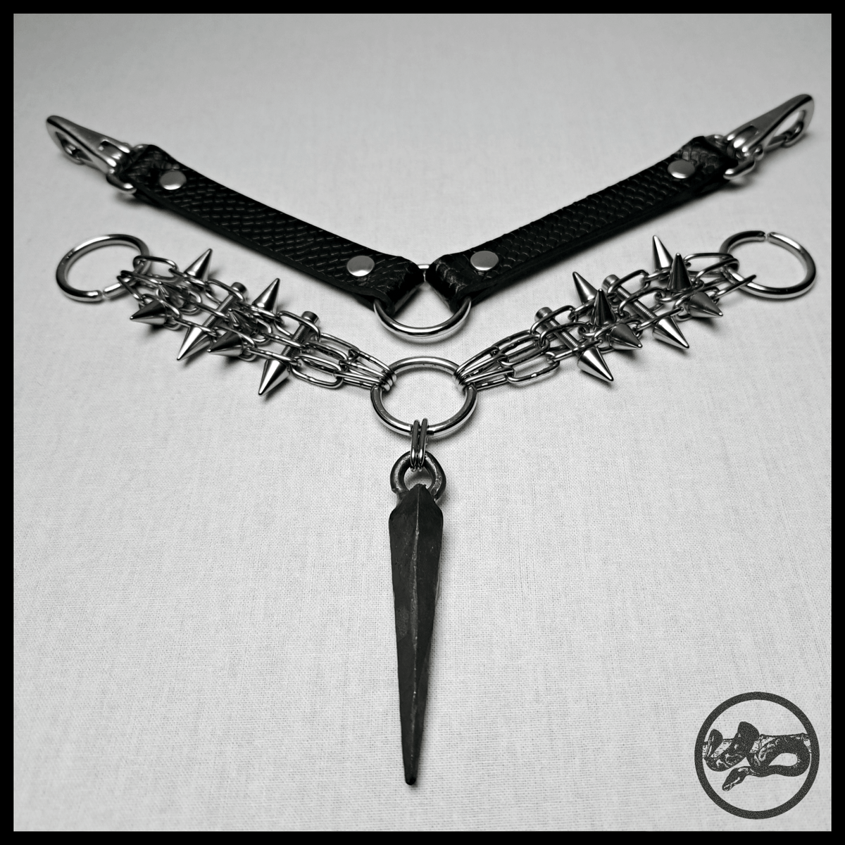 SARGNAGEL necklace laid out flat as a V: black embossed leather back strap with snap hooks above, spiked stainless chain arms and the forged coffin nail below. Handmade by skinpressedtight