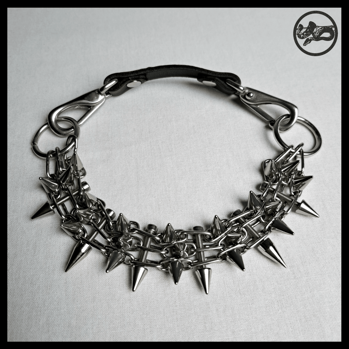 STŌRENFRIED choker laid flat from above: the spiked chain band, O-rings and the black leather back strap with snap hooks. Handmade by skinpressedtight