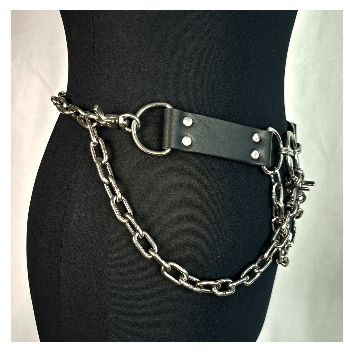 VIPERNZIRKEL – OPAQUE BLACK chain belt on a dress form, side: black leather tab, D-ring and heavy steel chain swagged round the hip. Handmade by skinpressedtight