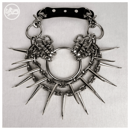 Brutalist necklace FEGEFEUER laid out flat in a front view, featuring studded stainless steel chains with long zinc alloy claw spikes, a large central O-ring, and a reclaimed leather neckpiece with stainless steel carbines, by skinpressedtight.