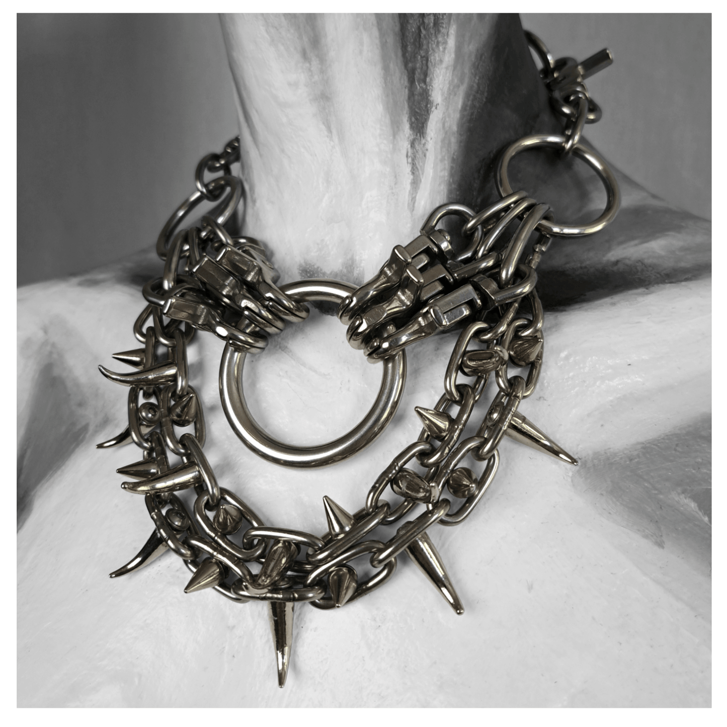 FEGEFLAMME brutalist necklace on mannequin, featuring studded stainless steel chains with small zinc alloy claw spikes, a central O-ring, and a reclaimed leather neckpiece fastened with stainless steel carbines — gothic handcrafted accessory by skinpressedtight.