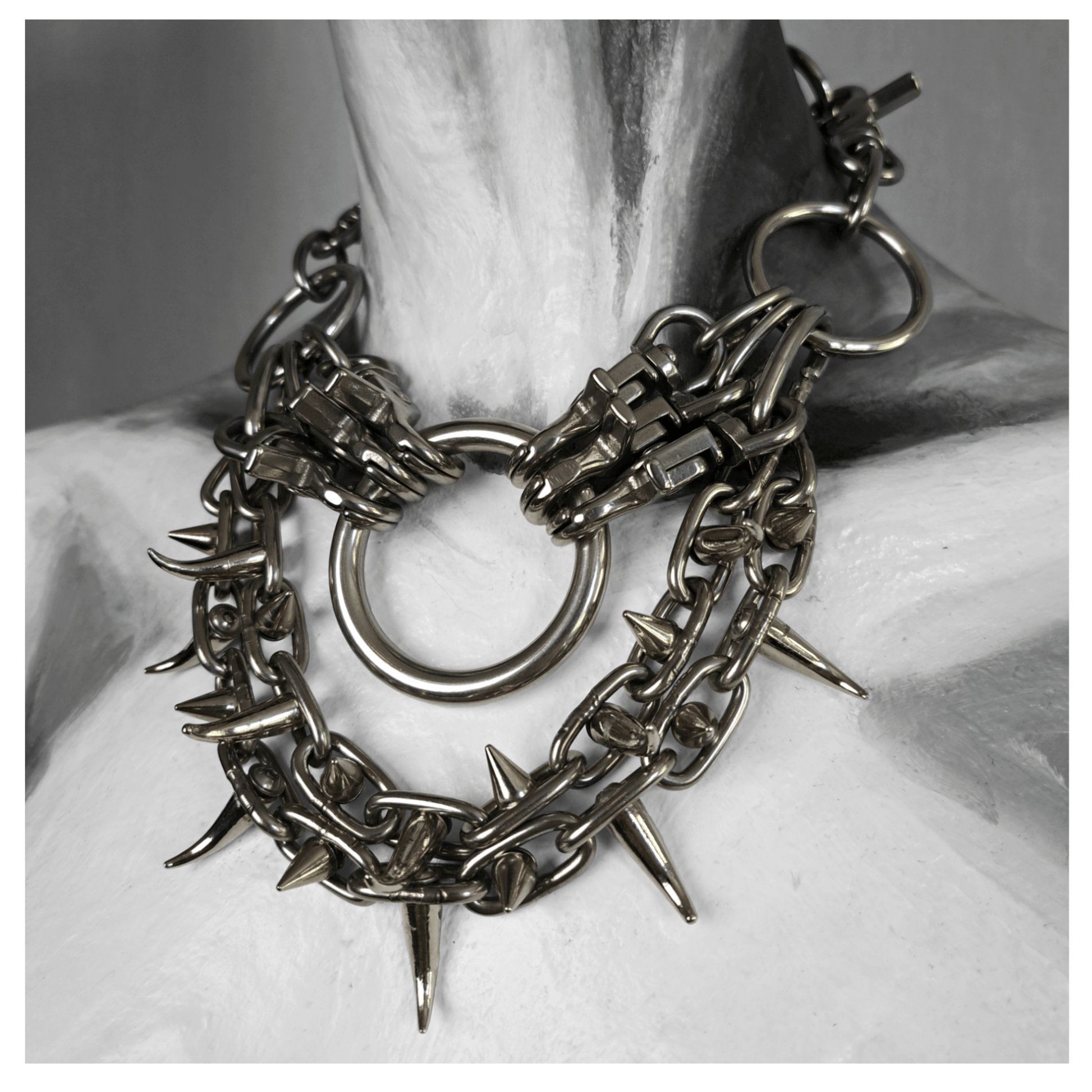 FEGEFLAMME brutalist necklace on mannequin, featuring studded stainless steel chains with small zinc alloy claw spikes, a central O-ring, and a reclaimed leather neckpiece fastened with stainless steel carbines — gothic handcrafted accessory by skinpressedtight.