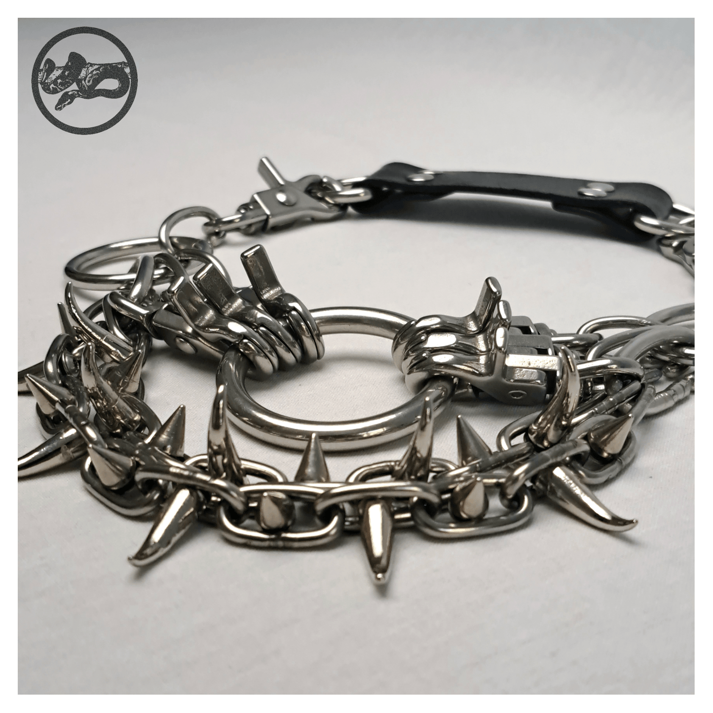 Detail view of FEGEFLAMME brutalist necklace on a white background, highlighting studded stainless steel chains with small zinc alloy claw spikes, central O-ring, and reclaimed leather neckpiece with stainless steel carbines — gothic handcrafted accessory by skinpressedtight.