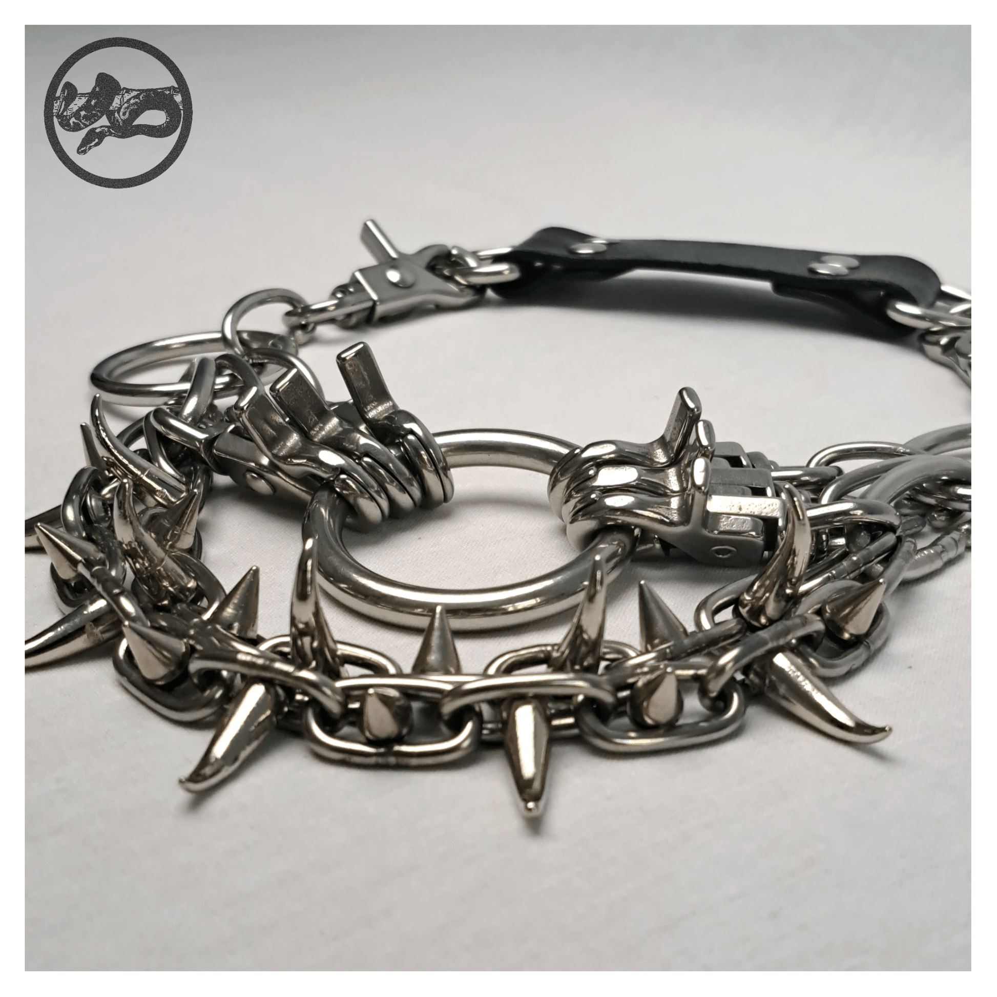 Detail view of FEGEFLAMME brutalist necklace on a white background, highlighting studded stainless steel chains with small zinc alloy claw spikes, central O-ring, and reclaimed leather neckpiece with stainless steel carbines — gothic handcrafted accessory by skinpressedtight.