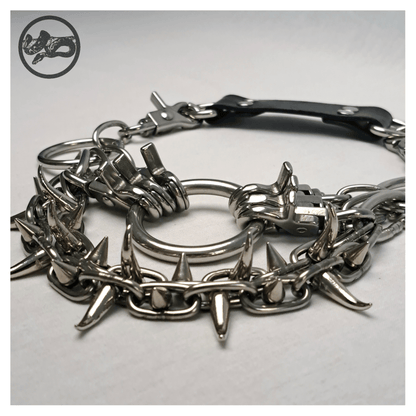 Detail view of FEGEFLAMME brutalist necklace on a white background, highlighting studded stainless steel chains with small zinc alloy claw spikes, central O-ring, and reclaimed leather neckpiece with stainless steel carbines — gothic handcrafted accessory by skinpressedtight.
