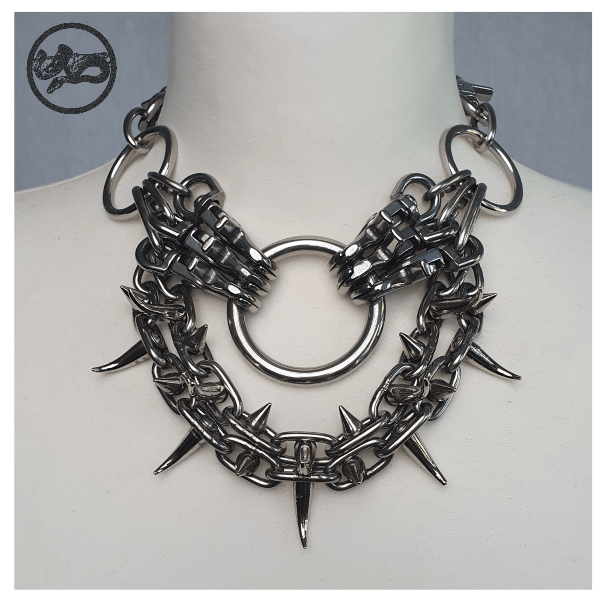 FEGEFLAMME brutalist necklace on a white mannequin, front view showing studded stainless steel chains with small zinc alloy claw spikes, central O-ring, and reclaimed leather neckpiece secured with stainless steel carbines — gothic handcrafted accessory by skinpressedtight.