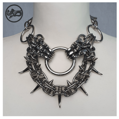 FEGEFLAMME brutalist necklace on a white mannequin, front view showing studded stainless steel chains with small zinc alloy claw spikes, central O-ring, and reclaimed leather neckpiece secured with stainless steel carbines — gothic handcrafted accessory by skinpressedtight.