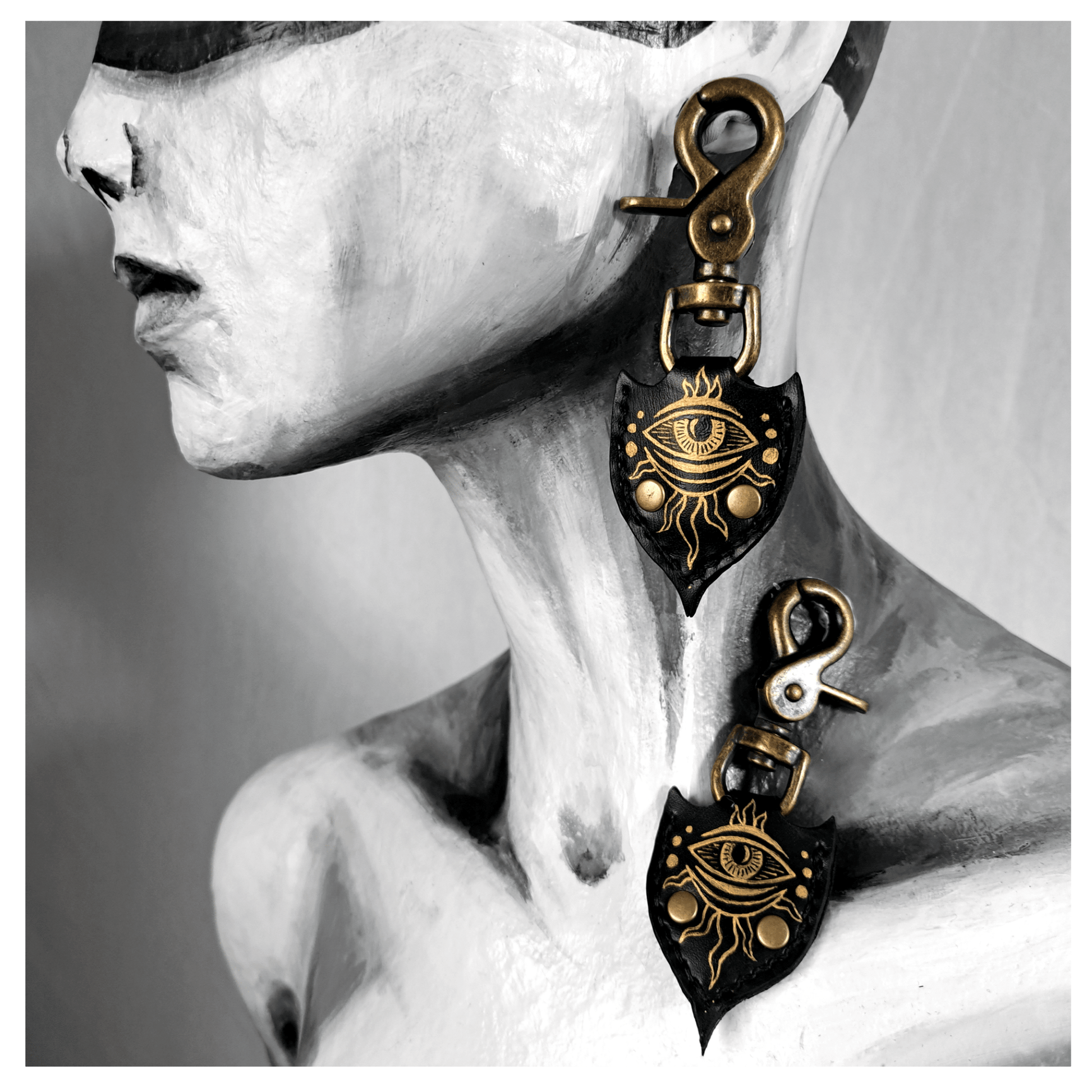 JOTKAELL spearhead-shaped earrings and ear charms displayed on mannequin, featuring leather pieces with handpainted golden eyes and tentacle ornaments, attached with brass carbines — gothic handcrafted accessories by skinpressedtight.