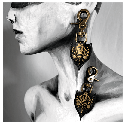 JOTKAELL spearhead-shaped earrings and ear charms displayed on mannequin, featuring leather pieces with handpainted golden eyes and tentacle ornaments, attached with brass carbines — gothic handcrafted accessories by skinpressedtight.