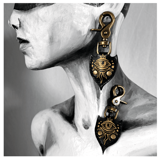 JOTKAELL spearhead-shaped earrings and ear charms displayed on mannequin, featuring leather pieces with handpainted golden eyes and tentacle ornaments, attached with brass carbines — gothic handcrafted accessories by skinpressedtight.