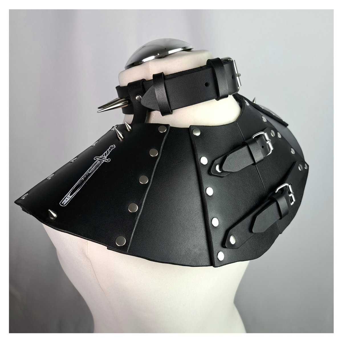 BLUTSPUR leather gorget from the back on a dress form: buckled straps closing the riveted panels, a white hand-painted sword on the leather. Handmade by skinpressedtight