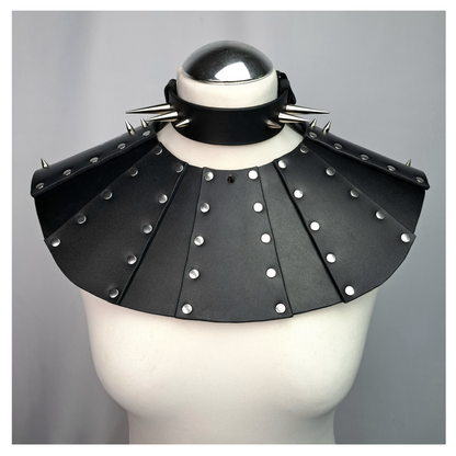 BLUTSPUR leather gorget on a white dress form, front: radial black leather armour panels studded with silver rivets and a black collar with long cone spikes. Handmade by skinpressedtight