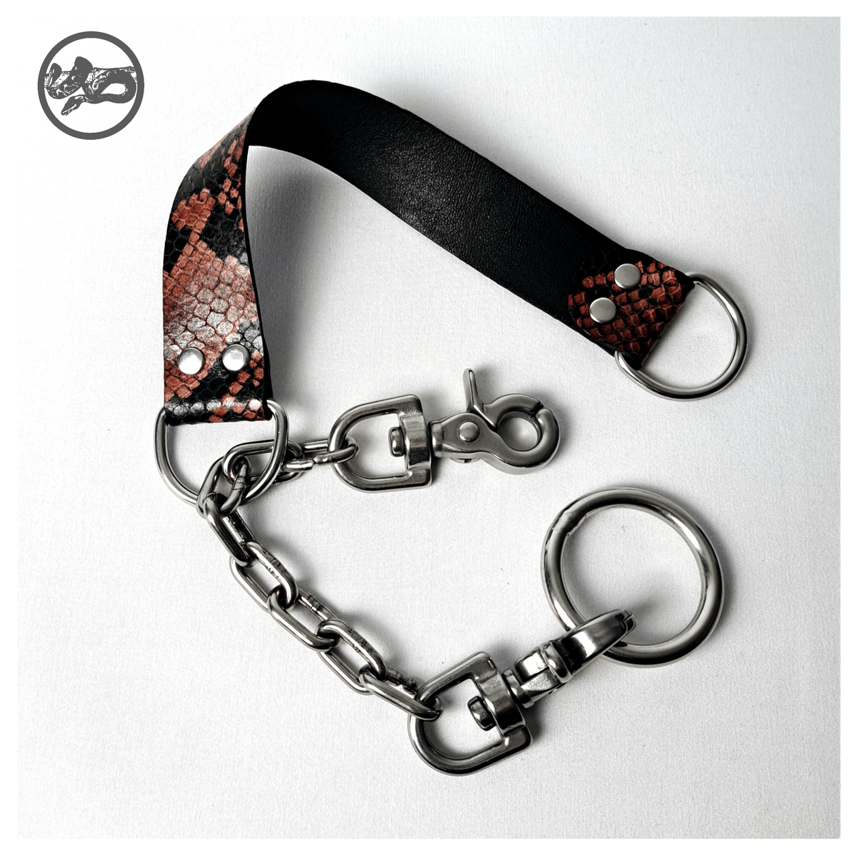 BOAKAPITEL – I. RED PYTHON choker open on white: one scissor carabiner unclipped from the O-ring, showing the chain running through the D-ring of the python-print leather band. Handmade by skinpressedtight