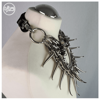 FEGEFEUER necklace on a white dress form, side view: the black leather strap around the neck clips into a steel ring at the shoulder, and the spiked chain front hangs heavy over the chest. Handmade by skinpressedtight