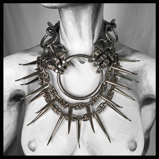 FEGEFEUER spiked necklace worn on a mannequin, black-and-white front view: a huge stainless steel O-ring and carabiner clusters surrounded by a halo of long curved spikes on heavy chain. Brutalist goth statement jewelry by skinpressedtight
