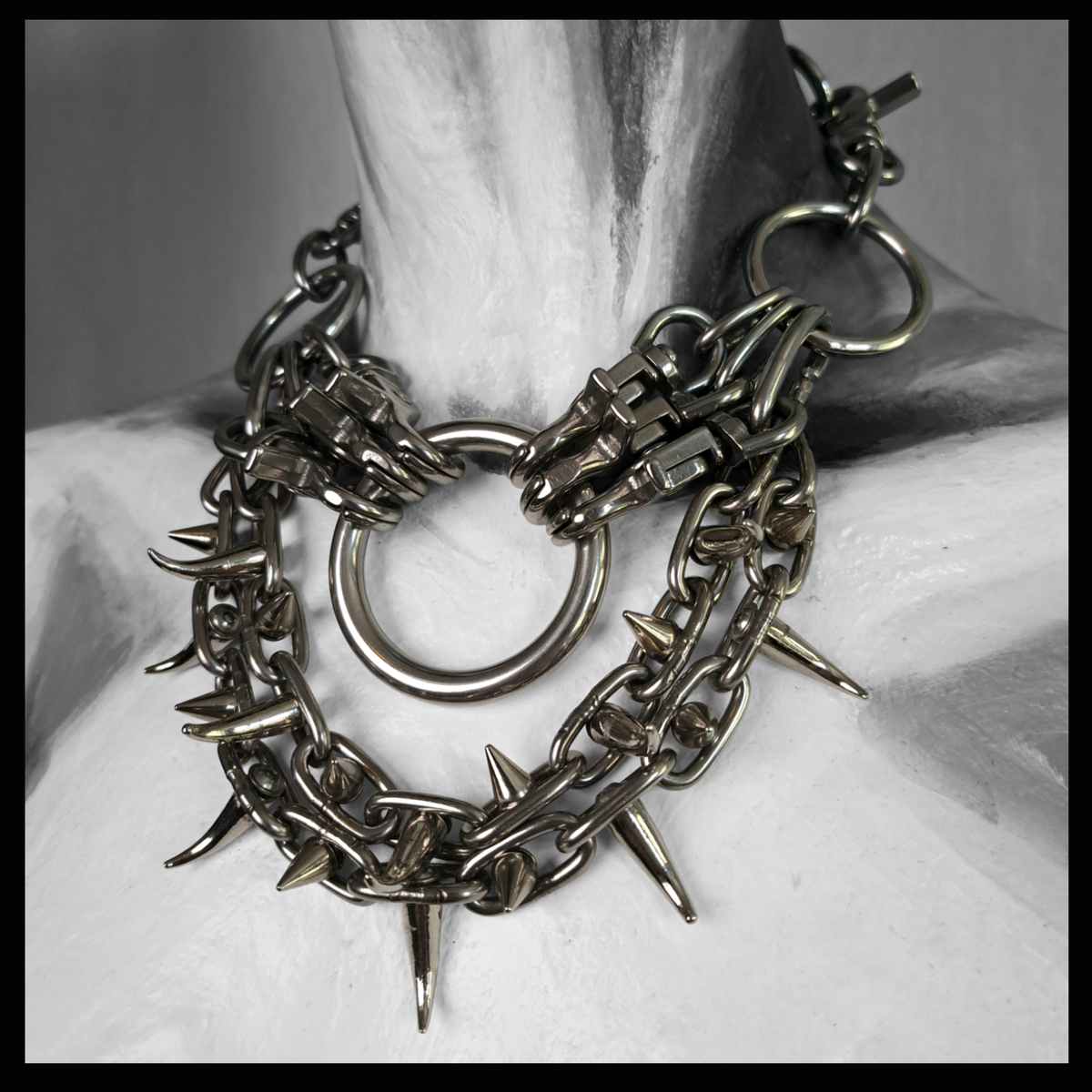 FEGEFLAMME statement necklace worn on a painted mannequin, black and white: a large stainless O-ring between two clusters of snap hooks, with two swags of chain set with spikes and claw studs below. Handmade by skinpressedtight