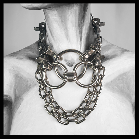 FLĀCHENBRAND chain necklace worn on a painted mannequin, black and white: three interlocked stainless rings at the throat held by scissor carabiners, heavy chain swags cascading onto the chest. Handmade by skinpressedtight
