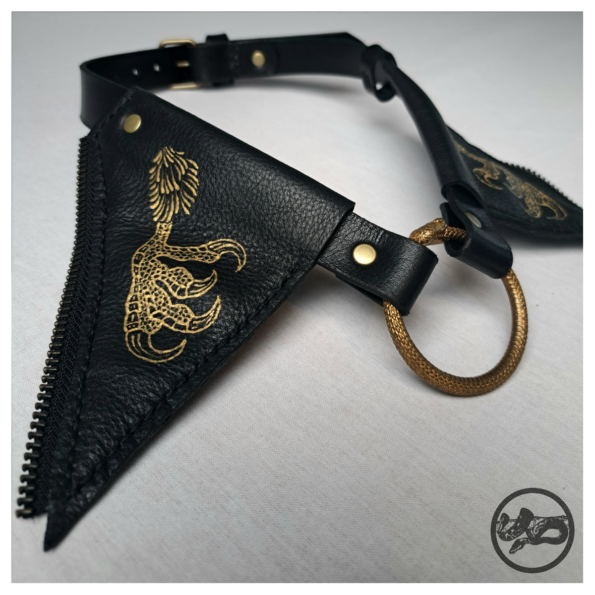 FLATTERTIER – BABA JAGA close-up: a gold hand-painted chicken leg and clawed foot on a pointed black leather flap, edged with zip teeth, and the brass ouroboros ring. Handmade by skinpressedtight