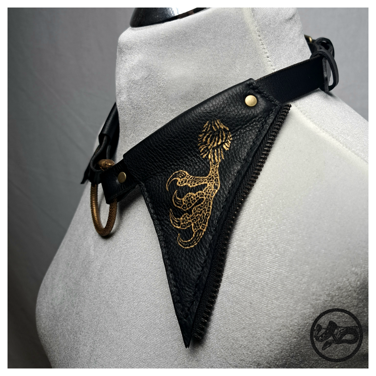 FLATTERTIER – BABA JAGA leather collar necklace on a dress form, three-quarter view: black leather flap with a gold-painted chicken foot, zip-tooth edging and the brass ring. Handmade by skinpressedtight