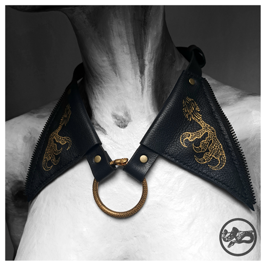 FLATTERTIER – BABA JAGA leather collar necklace worn on a painted mannequin: two pointed black leather flaps hand-painted with gold chicken feet, joined at the throat by a brass snake ring. Handmade by skinpressedtight