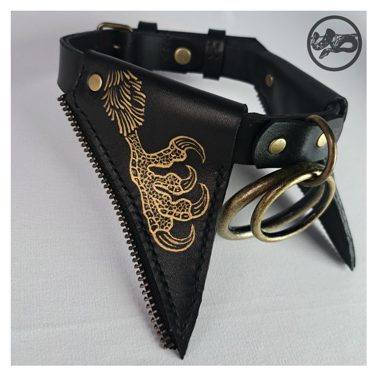 FLEDERTIER – BABA JAGA leather choker close-up: a gold-painted chicken leg and clawed foot on a pointed black leather flap edged with bronze zip teeth, brass double ring beside it. Handmade by skinpressedtight