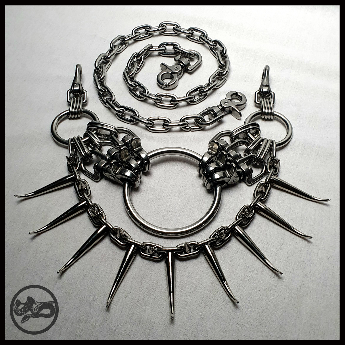 MYRAPOD – SPINNENLĀUFER spiked chain belt laid out flat: central O-ring, scissor carabiner clusters, a chain swag of curved horn spikes and small cone spikes, waist chain coiled above. Handmade by skinpressedtight
