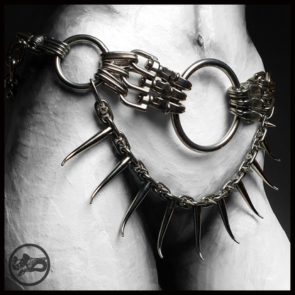 MYRAPOD – SPINNENLĀUFER spiked chain belt worn at the hips, black and white: large stainless ring and carabiner clusters, with a swag of long curved horn spikes hanging below like insect legs. Handmade by skinpressedtight