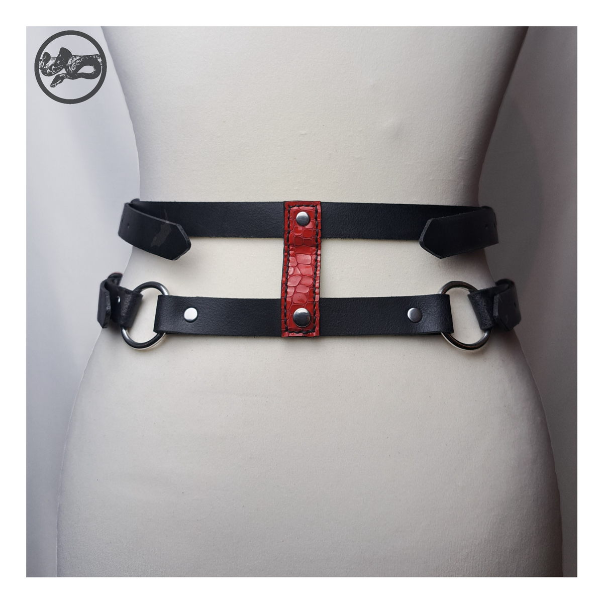 PURGATORIUM – DĀMONROT harness belt from the back on a dress form: two black straps joined by a red leather connector and O-rings. Handmade by skinpressedtight