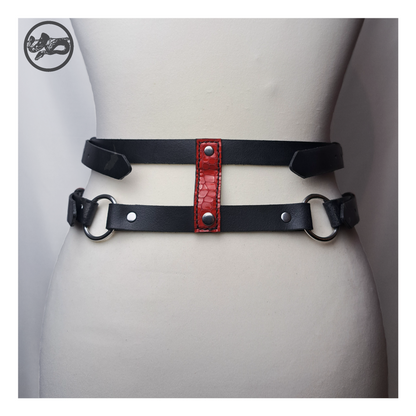 PURGATORIUM – DĀMONROT harness belt from the back on a dress form: two black straps joined by a red leather connector and O-rings. Handmade by skinpressedtight