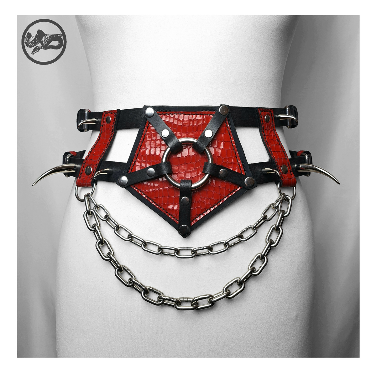 PURGATORIUM – DĀMONROT harness belt on a white dress form, front: glossy red leather pentagram around a stainless ring, curved spikes and two swags of chain. Handmade by skinpressedtight