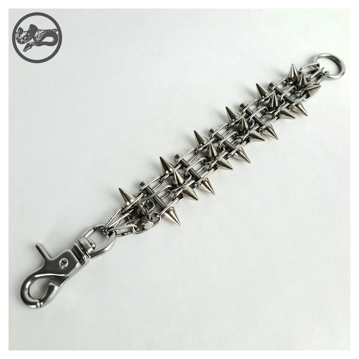 SCHALTKREIS spiked bracelet open on white, front: three strands of fine stainless chain joined by screw rungs, small cone spikes along the band, scissor carabiner at one end and O-ring at the other. Handmade by skinpressedtight