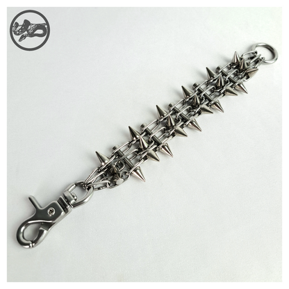 SCHALTKREIS spiked bracelet open on white, front: three strands of fine stainless chain joined by screw rungs, small cone spikes along the band, scissor carabiner at one end and O-ring at the other. Handmade by skinpressedtight