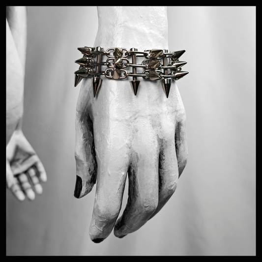 SCHALTKREIS spiked bracelet worn on a painted mannequin's wrist, black and white: a ladder band of fine stainless steel chain with rows of small cone spikes. Handmade by skinpressedtight