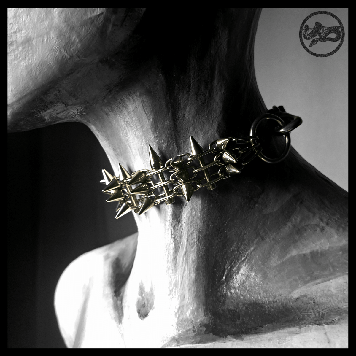 STŌRENFRIED spiked chain choker worn on a painted mannequin, three-quarter view: a dense band of stainless chain bristling with cone spikes, black leather strap at the back. Handmade by skinpressedtight