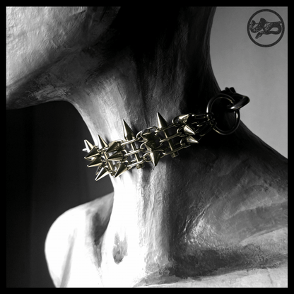 STŌRENFRIED spiked chain choker worn on a painted mannequin, three-quarter view: a dense band of stainless chain bristling with cone spikes, black leather strap at the back. Handmade by skinpressedtight