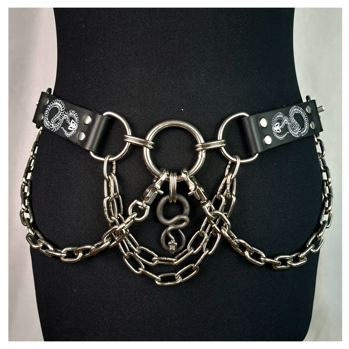 VIPERNZIRKEL – BONES chain belt on a black dress form, front: white snake skeletons on the leather tabs, steel O-rings, chain swags and a silver snake pendant. Handmade by skinpressedtight